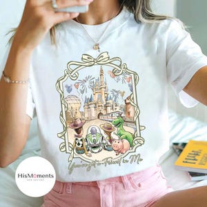 Peut inclure: T-shirt blanc avec une illustration &agrave; l'aquarelle d'un ch&acirc;teau, de feux d'artifice et de personnages de dessins anim&eacute;s. Le motif comprend Woody, Buzz l'&Eacute;clair, Rex et Hamm. Le texte "You've got a Friend in Me" est &eacute;crit en dessous.
