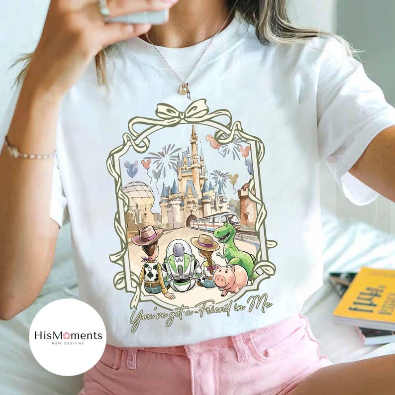 Peut inclure: T-shirt blanc avec une illustration &agrave; l'aquarelle d'un ch&acirc;teau, de feux d'artifice et de personnages de dessins anim&eacute;s. Le motif comprend Woody, Buzz l'&Eacute;clair, Rex et Hamm. Le texte "You've got a Friend in Me" est &eacute;crit en dessous.