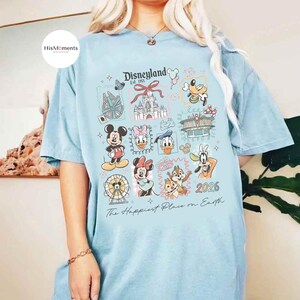 Peut inclure: T-shirt bleu clair avec un motif Disneyland, repr&eacute;sentant Mickey Mouse, Minnie Mouse et Donald Duck. Le t-shirt affiche le texte "Disneyland Est. 1955" et "The Happiest Place on Earth."
