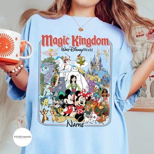 Puede incluir: Camiseta azul claro con un dise&ntilde;o de personajes de Disney y el texto "Magic Kingdom Walt Disney World". El dise&ntilde;o incluye a Mickey y Minnie Mouse, y otros personajes. La palabra "Name" tambi&eacute;n es visible.