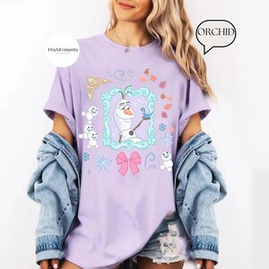 May include: A light purple t-shirt featuring a cartoon image of Olaf from Frozen, holding a blue bird. The design includes snowflakes, a pink bow, and the text "HisMoments" on the left side. The word "ORCHID" is in a speech bubble on the right.