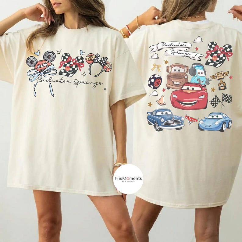 Może przedstawiać: Kremowa koszulka z nadrukiem z przodu przedstawiającym uszy Myszki Miki, koła samochod&oacute;w wyścigowych i napis "Radiator Springs". Tył koszulki przedstawia r&oacute;żne kresk&oacute;wkowe samochody i napis "Radiator Springs".