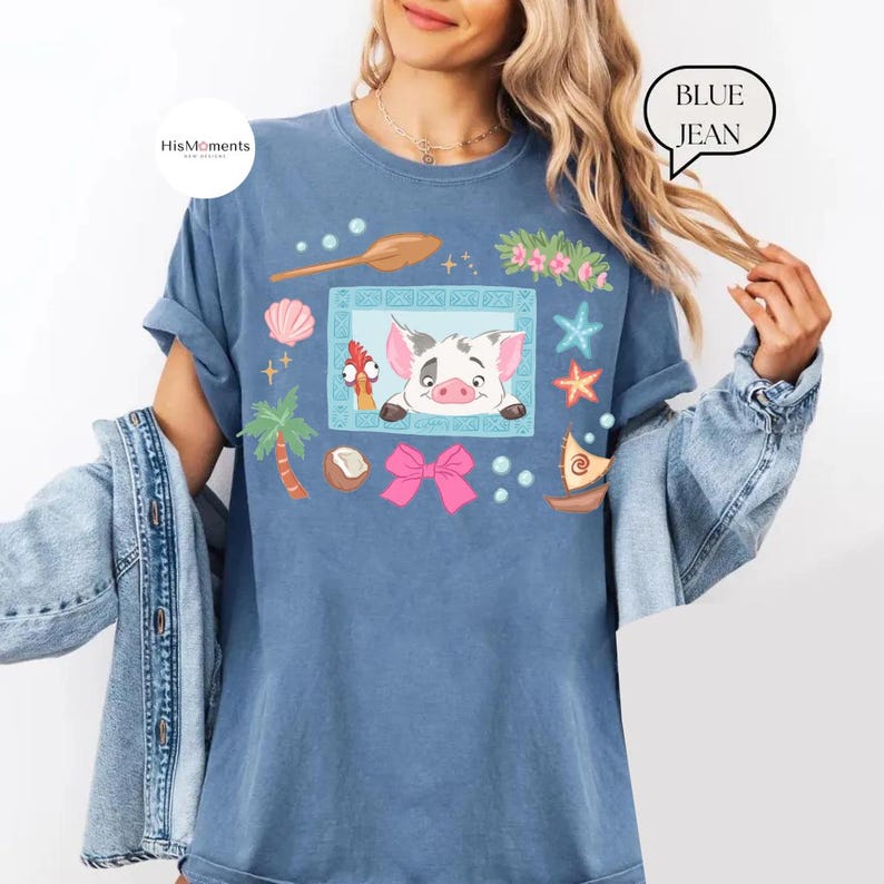 May include: Blue jean t-shirt featuring a cartoon illustration of a pig and a rooster, surrounded by tropical elements like seashells, starfish, and a pink bow. The shirt has a relaxed fit and the text "BLUE JEAN" is printed on the upper right.