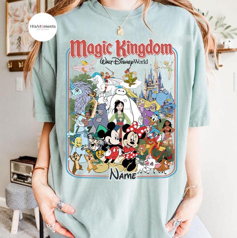 Puede incluir: Camiseta azul claro con un gr&aacute;fico colorido de personajes de Disney, incluyendo Mickey y Minnie Mouse, con el texto "Magic Kingdom Walt Disney World" en rojo y blanco. La palabra "Name" tambi&eacute;n es visible.