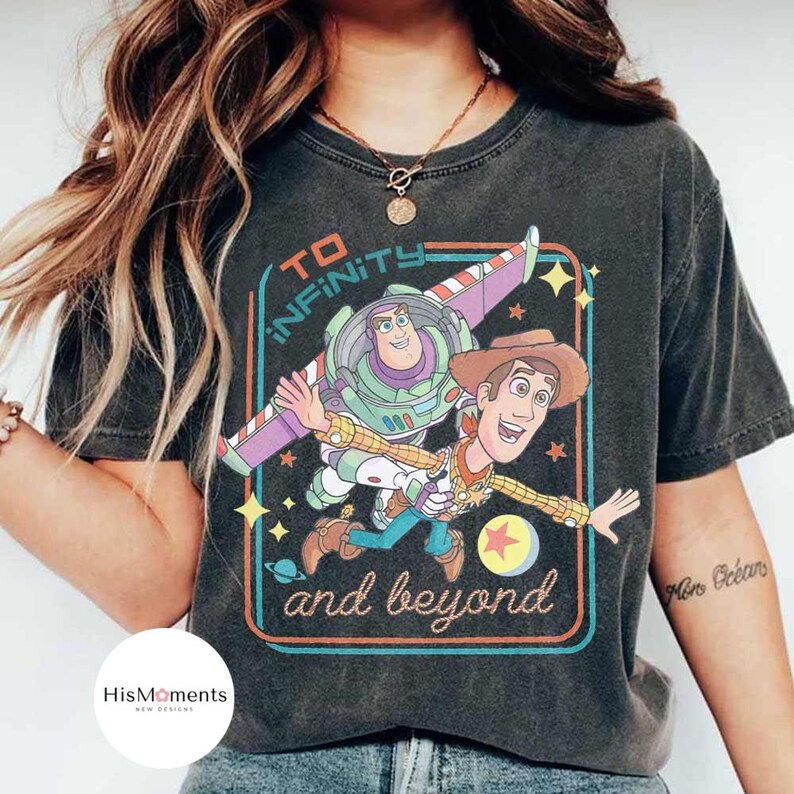 May include: Dark gray t-shirt featuring a colorful graphic of Buzz Lightyear and Woody from Toy Story, with the text "TO INFINITY and beyond" in a retro design. The shirt has a vintage, worn look.