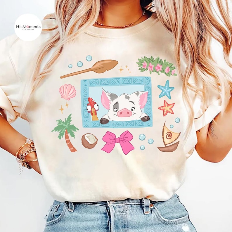 May include: Cream-colored t-shirt featuring a cartoon illustration of a pig and a rooster in a blue frame, surrounded by tropical elements like a palm tree, seashells, and a pink bow. The shirt has the text "HisMoments" on the upper left.