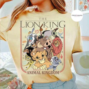 May include: Yellow t-shirt featuring a graphic of characters from The Lion King, including Simba, Timon, Pumbaa, and Mufasa. The text "THE LION KING ANIMAL KINGDOM" is printed above and below the characters in a rectangular frame.