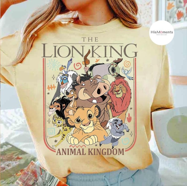 May include: Yellow t-shirt featuring a graphic of characters from The Lion King, including Simba, Timon, Pumbaa, and Mufasa. The text "THE LION KING ANIMAL KINGDOM" is printed above and below the characters in a rectangular frame.