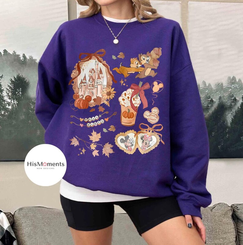 Op de afbeelding: Een paarse sweatshirt met Disney-thema herfstafbeeldingen. Het ontwerp bevat een kasteel, Knabbel en Babbel, Mickey en Minnie Mouse, een pumpkin spice latte en herfstbladeren. De tekst "HisMoments new designs" staat op de sweatshirt.