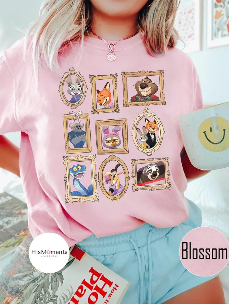 Puede incluir: Camiseta rosa claro con retratos enmarcados en oro de personajes de dibujos animados. La camiseta tiene la palabra "Blossom" impresa. La marca "HisMoments" tambi&eacute;n est&aacute; impresa en la camiseta. La camiseta es de corte holgado.