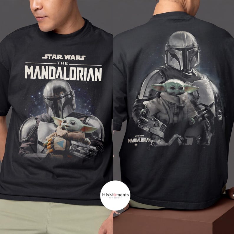 May include: Black t-shirt featuring the text "STAR WARS THE MANDALORIAN" above an image of The Mandalorian and Grogu. The back of the shirt shows the Mandalorian holding Grogu. The shirt is made of a soft material.