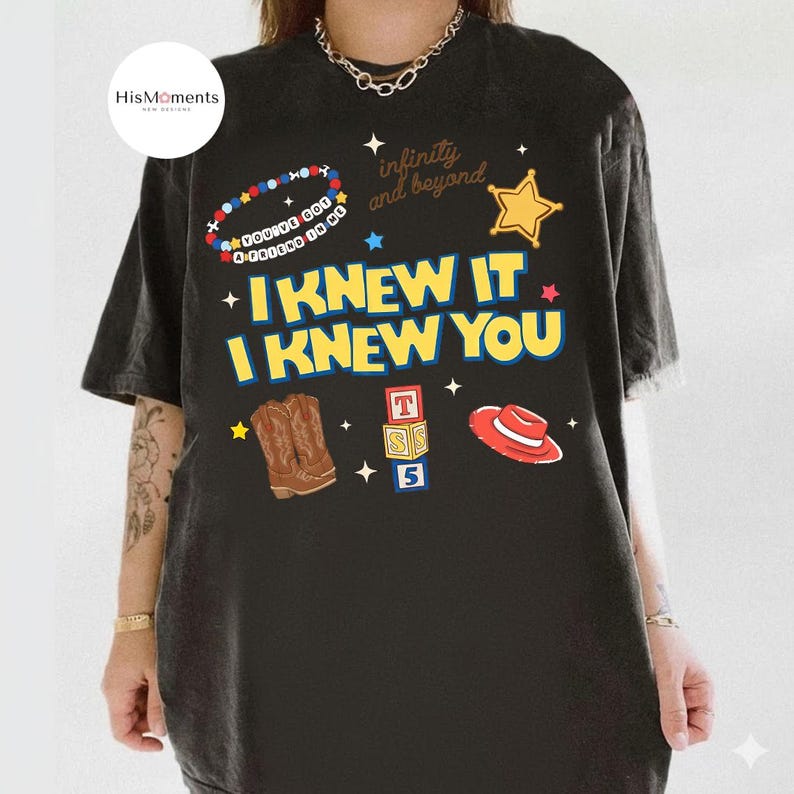 K&ouml;nnte beinhalten: Ein schwarzes T-Shirt mit einem Grafikdruck mit dem Text I KNEW IT I KNEW YOU, infinity and beyond und YOU'VE GOT A FRIEND IN ME. Das Design enth&auml;lt Illustrationen eines Sheriffsterns, Cowboystiefeln, Buchstabenw&uuml;rfeln und einem roten Hut.