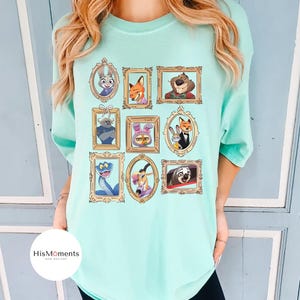 Puede incluir: Camiseta de color verde azulado claro con retratos de dibujos animados enmarcados de varios animales. Los retratos est&aacute;n en marcos dorados ornamentados. La camiseta tiene un corte holgado y mangas cortas. El logo de la marca "HisMoments" es visible.