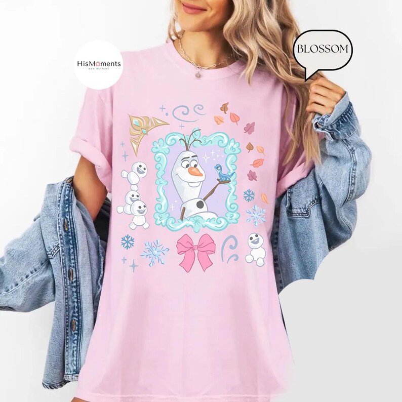May include: A light pink t-shirt featuring a cartoon image of Olaf from Frozen, surrounded by snowflakes, leaves, and a pink bow. The shirt has the text "HisMoments" on the upper left and "BLOSSOM" on the upper right.