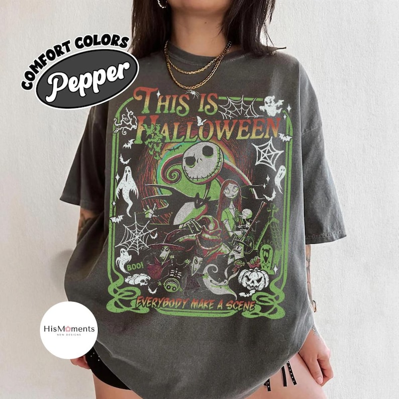 K&ouml;nnte beinhalten: Dunkelgraues T-Shirt mit einem Halloween-Motiv, das Jack Skellington und Sally zeigt. Der Text "THIS IS HALLOWEEN" steht &uuml;ber der Grafik, darunter "EVERYBODY MAKE A SCENE". Das Shirt hat einen Vintage-Look mit gr&uuml;nen und roten Farbt&ouml;nen.