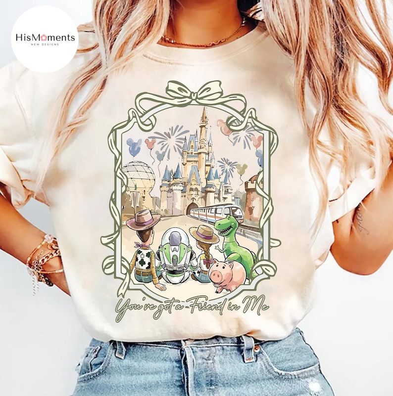 Peut inclure: T-shirt cr&egrave;me avec une illustration encadr&eacute;e des personnages de Toy Story devant un ch&acirc;teau, des feux d'artifice et un train. Le texte "You've got a Friend in Me" est &eacute;crit en dessous. Le t-shirt a un col rond.