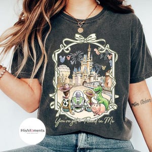 Peut inclure: T-shirt gris fonc&eacute; avec une illustration color&eacute;e de personnages Disney devant un ch&acirc;teau. L'image comprend le texte "You've got a Friend in Me" dans un cadre d&eacute;coratif. Le t-shirt est con&ccedil;u pour un usage d&eacute;contract&eacute;.