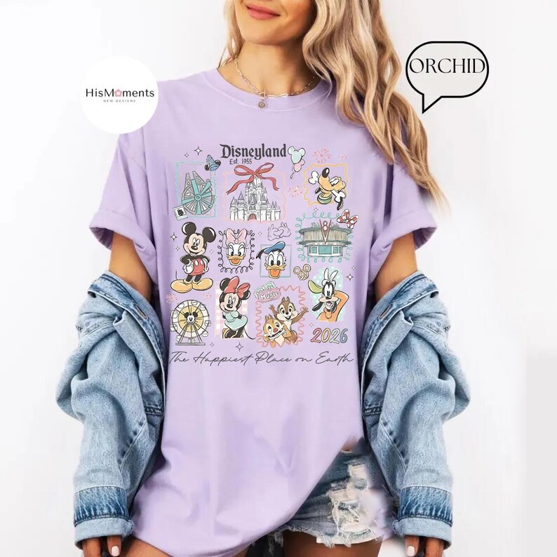 Peut inclure: T-shirt lilas avec un motif Disneyland, repr&eacute;sentant des personnages de dessins anim&eacute;s et des monuments embl&eacute;matiques. Le t-shirt affiche le texte "Disneyland Est. 1955" et "The Happiest Place on Earth" avec l'ann&eacute;e 2026.