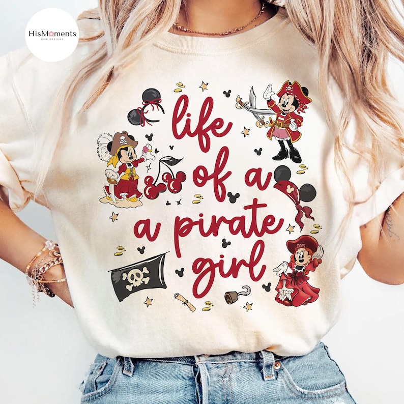 May include: Cream-colored t-shirt with a red graphic that reads "life of a pirate girl." The design features cartoon pirate characters, cherries, stars, a skull and crossbones flag, and a scroll.