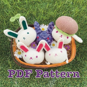 May include: A basket filled with several crocheted bunny toys in various colors. The bunnies are white, purple, and one with a burger hat. The text "PDF Pattern" is at the bottom of the image. Daisies and other flowers are scattered around the basket.