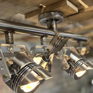 May include: A silver track lighting system with three spotlights. The spotlights are adjustable and have a brushed metal finish. The track is mounted to a wooden ceiling.