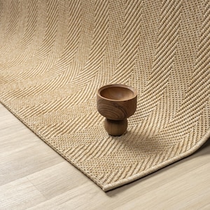 Könnte beinhalten: Ein beigefarbener gewebter Teppich mit Fischgrätenmuster. Eine kleine, runde Holzschale steht auf dem Teppich. Der Teppich hat eine gebogene Kante und liegt auf einem hellen Holzboden.