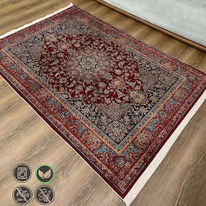 Puede incluir: Una alfombra roja, azul y dorada con un patrón y flecos blancos. La alfombra tiene un diseño persa tradicional.