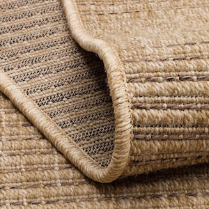 Puede incluir: Primer plano de una alfombra beige enrollada con una textura tejida. La alfombra tiene un borde beige y una mezcla de hilos marrón claro y oscuro que crean un patrón sutil. Las fibras de la alfombra son visibles, lo que sugiere un material natural.