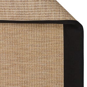 May include: Close-up of a tan and black rug. The rug features a woven texture with vertical lines in shades of tan and brown. A thick black border frames the edge of the rug, creating a defined edge.