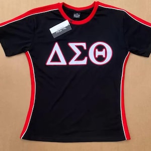 May include: Black athletic shirt with red and white trim. The shirt features the Greek letters &Delta;&Sigma;&Theta; in white, outlined in red. A tag is attached to the shirt.