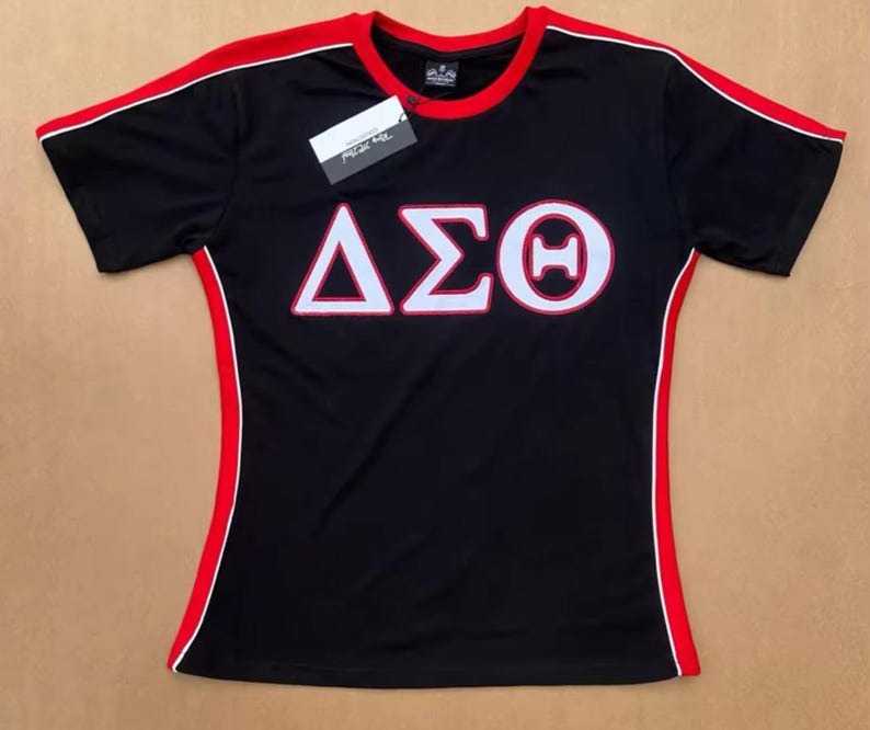 May include: Black athletic shirt with red and white trim. The shirt features the Greek letters &Delta;&Sigma;&Theta; in white, outlined in red. A tag is attached to the shirt.