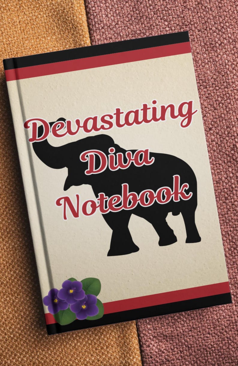 Op de afbeelding: Een notitieboek met de woorden "Devastating Diva Notebook" in rood script, met een zwart olifant silhouet. Het notitieboek heeft een cr&egrave;mekleurige kaft met rode en zwarte randen en een tros paarse bloemen.