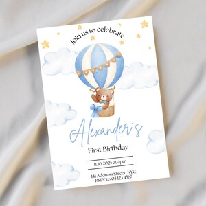 May include: A blue and white hot air balloon with a teddy bear in the basket. The balloon is surrounded by clouds and stars. The text "Join us to celebrate Alexander's First Birthday" is printed on the card. The date and time of the party are also included, along with the address and RSVP information.