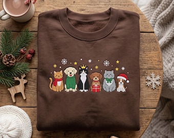 May include: A dark brown crewneck sweatshirt featuring a graphic print of six cartoon animals including cats and dogs wearing holiday accessories like a red scarf, green sweater, gold crown, red gift box, green bow, and a red Santa hat.
