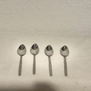 Könnte beinhalten: Vier silberne Teelöffel in einer Reihe auf einer weißen Oberfläche angeordnet.