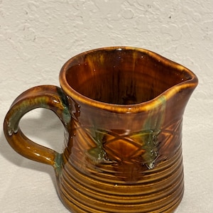 Könnte beinhalten: Ein brauner Keramik-Krug mit grüner Glasur und einem Henkel. Der Krug hat ein geripptes Design und ein Rautenmuster.