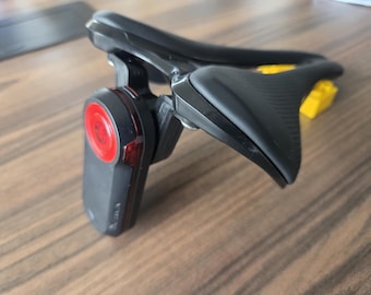 May include: Black and red electronic device with a curved design. The device has a red circular element and a yellow component. The object is on a wooden surface.