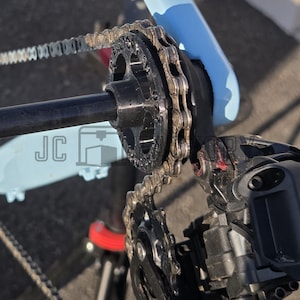 Op de afbeelding: Close-up van een fietsaandrijving met een zwarte ketting, tandwielen en derailleur. Het fietsframe is lichtblauw. De ketting verbindt de tandwielen en de derailleur, essentieel voor schakelen en krachtoverbrenging.