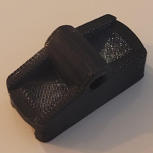 Könnte beinhalten: Ein schwarzes, 3D-gedrucktes Objekt aus Kunststoff mit einem Loch in der Mitte und einem erhöhten Abschnitt oben.