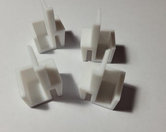May include: Four white plastic corner brackets with a square shape and a small lip on each side. The brackets are designed to be used for joining two pieces of wood or other materials at a 90-degree angle.