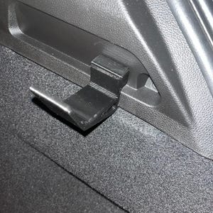 Peut inclure: Un crochet en plastique noir fixé à l'intérieur du coffre d'une voiture.