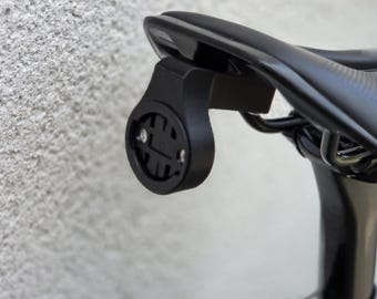 May include: Black bicycle seat with a black bracket attached, designed to hold a cycling computer. The bracket is mounted to the seat post and features a round, recessed area with screw holes.