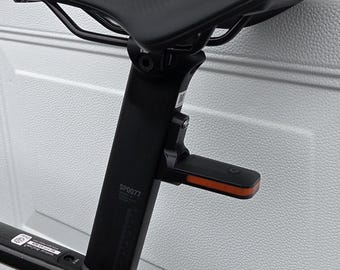 May include: A black bicycle seat and seat post with an integrated orange reflector. The seat has a textured surface and is mounted on a black post. The post has the text "SP0077".