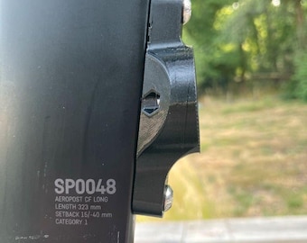 May include: Black bicycle seat post with a black bracket attached with silver bolts. The text "SP0048" is visible, along with other technical specifications including a length of 323 mm.