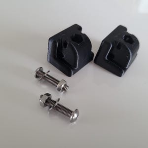 Op de afbeelding: Twee zwarte plastic 3D-geprinte beugels met twee zilveren schroeven en moeren.