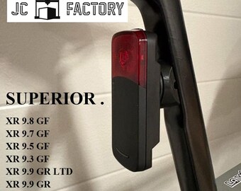 May include: A black and red bicycle tail light attached to a black seat post. The text "JC FACTORY" and "SUPERIOR" are visible. Below the text are model numbers including XR 9.8 GF and XR 9.7 GF.