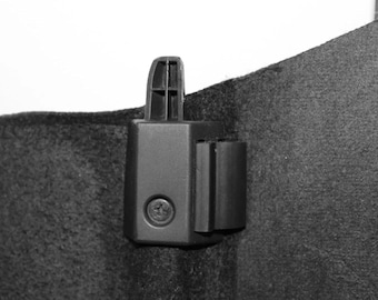 May include: A black plastic car part with a screw in the center. The part has a textured surface and a small rectangular tab on the side.