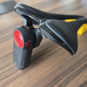 Peut inclure: Appareil électronique noir et rouge au design incurvé. L'appareil comporte un élément circulaire rouge et un composant jaune. L'objet est posé sur une surface en bois.