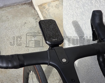 May include: Black bicycle handlebar with a mounted black Garmin device. The handlebar is wrapped in black tape. The image also shows a portion of a bicycle wheel and the text "JC FACTORY".
