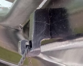 May include: Close-up of a black plastic component with a textured surface and a rope attached. The component appears to be part of a larger structure, possibly a vehicle or similar item. The rope is gray and appears to be made of woven fibers.